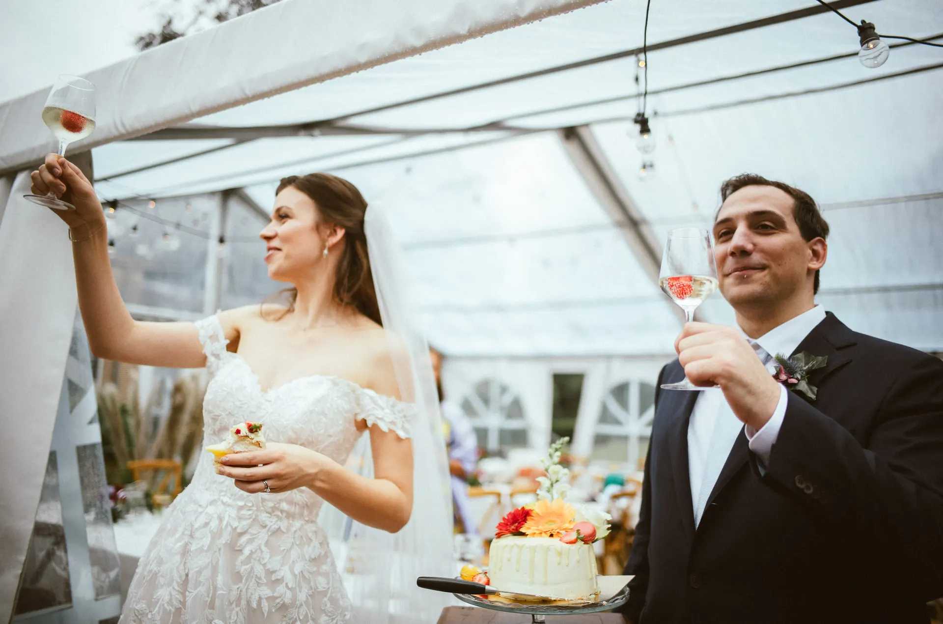 Newlyweds raising champagne glasses beside their wedding cake