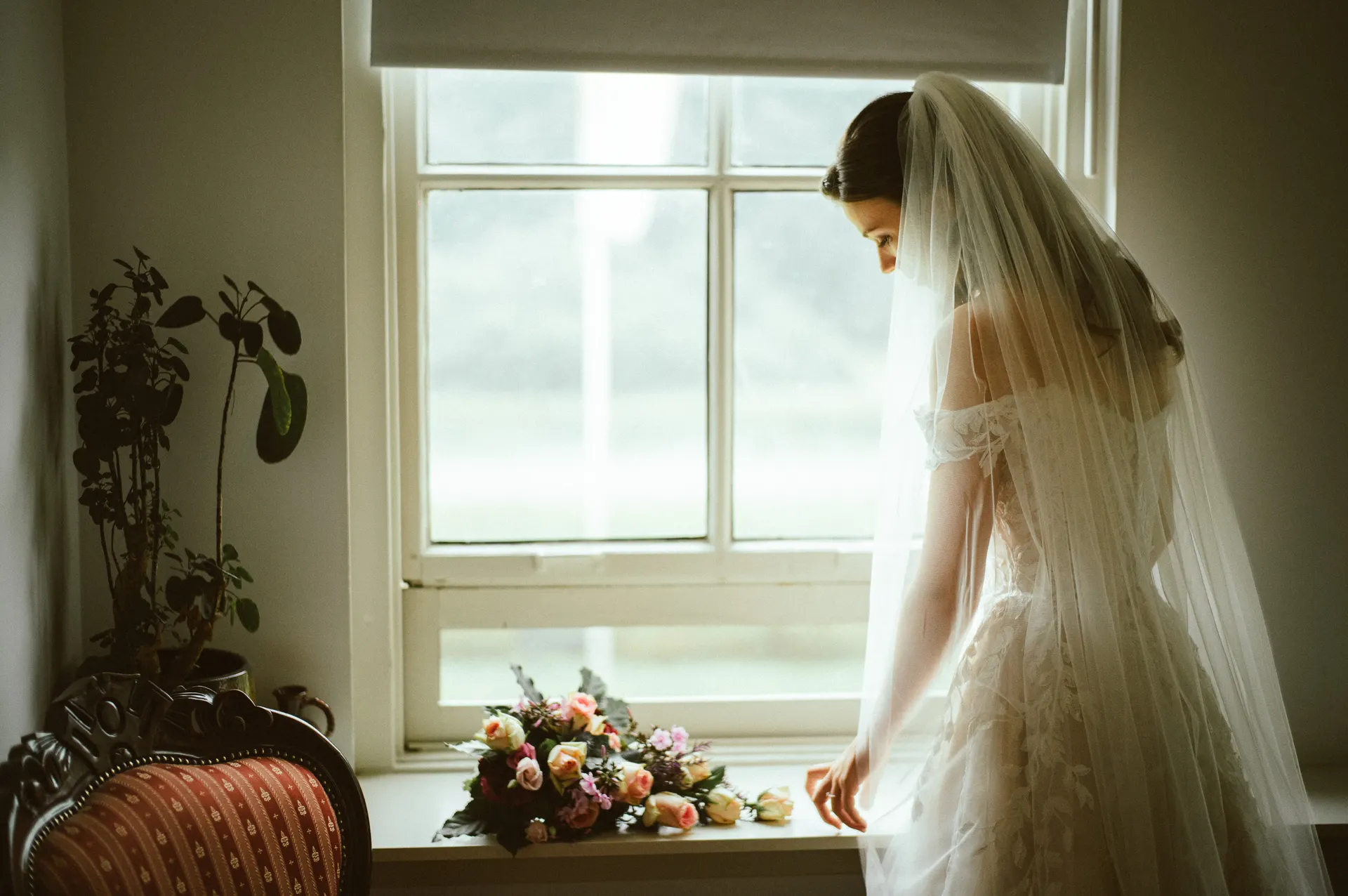 Bride standing in soft window light before her wedding ceremony
