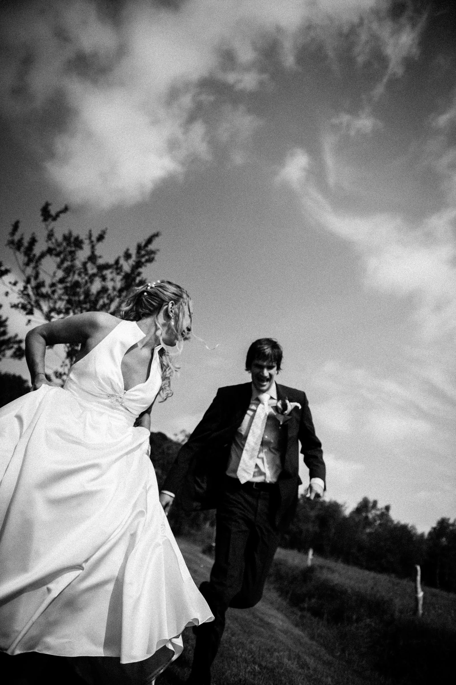 Black-and-white photograph of newlyweds walking together beneath an open sky